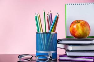 retour au concept de l'école. fournitures scolaires, livres et pomme sur fond rose. place pour le texte. photo