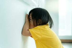 peu asiatique les enfants enfant en jouant cacher et chercher permanent suivant mur loger, adorable enfant ayant amusement dans le maison. content famille avoir amusement avec enfants, activité, apprentissage, activité, jeu, méditation photo