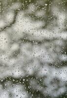 une photo de gouttes de pluie sur la vitre avec une vue floue des arbres verts en fleurs. image abstraite montrant des conditions météorologiques nuageuses et pluvieuses