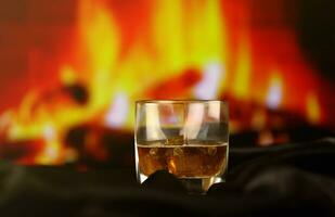 whisky ou whisky ou bourbon avec de la glace sur une surface en bois sur fond de cheminée. alcool d'élite de luxe dans un verre large. scène discrète photo