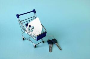 mini achats chariot avec une blanc maison et clés sur une bleu Contexte. le photo