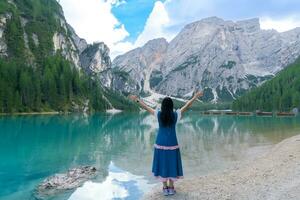 arrière vue de asiatique femme touristique permanent sur le côte de braies lac. dolomites, Italie. paysage avec fille, célèbre Lac avec magnifique réflexion dans eau, des arbres, ciel avec des nuages. Voyage. photo