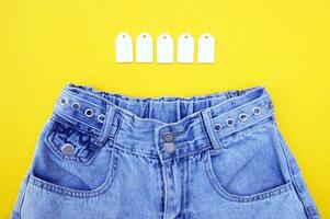 plat poser, détail de denim jeans avec Vide blanc Étiquettes sur Jaune Contexte. photo