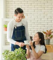 portrait jeune garçon fille couple asiatique portant un tablier. ils boivent une tasse de café chaud et aident à installer une petite plante sur une table en bois dans leur maison. pour la beauté avec un sourire éclatant heureux jeunes mariés photo