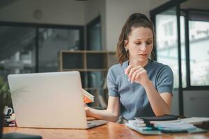 affaires femme séance à Bureau bureau et l'écriture Remarques dans une carnet tandis que parlant sur une vidéo appel réunion avec clients ou collègues de travail sur sa portable ordinateur. photo