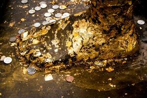 d'or feuille collé et thaïlandais une baignoire pièce de monnaie sur Bouddha pied statue photo