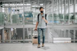homme asiatique avec masque facial avec bagages à l'aide d'un smartphone