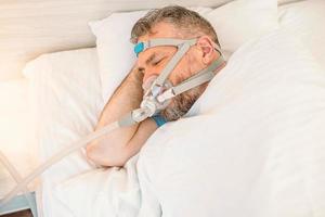 un homme endormi souffrant de problèmes respiratoires chroniques envisage d'utiliser une machine cpap au lit. soins de santé, thérapie de l'apnée obstructive du sommeil, cpap, concept de ronflement photo