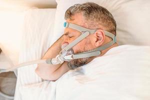 un homme endormi souffrant de problèmes respiratoires chroniques envisage d'utiliser une machine cpap au lit. soins de santé, thérapie de l'apnée obstructive du sommeil, cpap, concept de ronflement photo