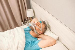 un homme endormi souffrant de problèmes respiratoires chroniques envisage d'utiliser une machine cpap au lit. soins de santé, thérapie de l'apnée obstructive du sommeil, cpap, concept de ronflement photo