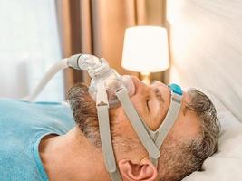 un homme endormi souffrant de problèmes respiratoires chroniques envisage d'utiliser une machine cpap au lit. soins de santé, thérapie de l'apnée obstructive du sommeil, cpap, concept de ronflement photo