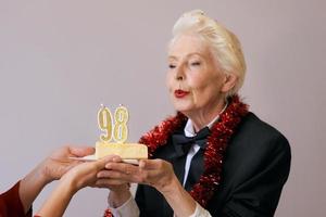 Heureuse femme de quatre-vingt-dix-huit ans élégante et joyeuse en costume noir célébrant son anniversaire avec un gâteau. mode de vie, positif, mode, concept de style photo