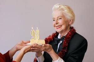 Heureuse femme de quatre-vingt-dix-huit ans élégante et joyeuse en costume noir célébrant son anniversaire avec un gâteau. mode de vie, positif, mode, concept de style photo