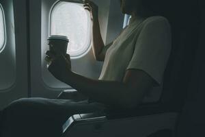 asiatique femme profiter jouit une café confortable vol tandis que séance dans le avion cabine, les passagers près le la fenêtre. photo