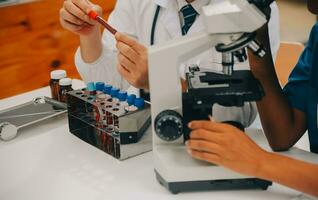 médical ouvrier dans laboratoire manteau et stérile masque, Faire une microscope une analyse tandis que sa collègue sont travail derrière photo