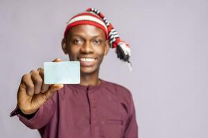 africain homme portant africain tenue robe en portant id carte moquer en haut des stands sur une gris studio mur . sélectif concentrer photo