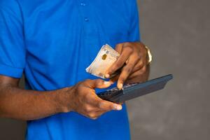 proche en haut main coup de un africain homme en portant certains argent et en utilisant une calculatrice photo
