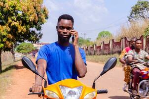 Jeune Beau africain motard fabrication appels tandis que attendre pour le sien client à arrivée photo