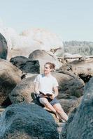 jeune homme regardant loin de la caméra en lisant un livre sur le rivage de la mer, espace de copie, confiance et concepts d'étude, avenir et auto-assistance