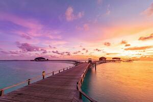 coucher de soleil sur l'île des maldives, complexe de villas sur l'eau de luxe et jetée en bois. beau ciel et nuages et fond de plage pour les vacances d'été et le concept de voyage photo