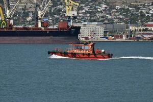 petit navire dans le Port de le service. rouge petit bateau. cargaison Port avec Port grues. mer baie et montagneux côte. photo