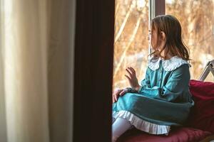 une pensif mignonne fille est assis et regards en dehors le fenêtre photo