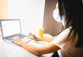 jeune femme caucasienne séduisante tient un stylo et écrit des notes devant un ordinateur portable dans une pièce confortable en arrière-plan. photo