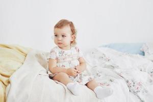 notion d'enfance. petite fille en robe mignonne implantation au lit jouant avec des jouets à la maison. chambre d'enfant vintage blanche photo