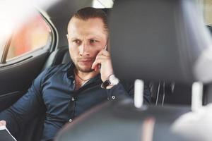 un homme d'affaires qui envoie un message à un smartphone et se dirige vers le siège arrière de la voiture. photo