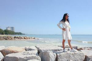 magnifique femme dans blanc robe permanent sur le pierre près le mer photo