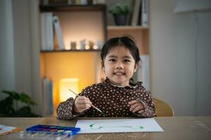 mignon petit bébé asiatique souriant peinture avec des peintures colorées à l'aquarelle. fille asiatique utilisant la couleur de dessin au pinceau. concept de mode de vie d'activité de bébé. photo