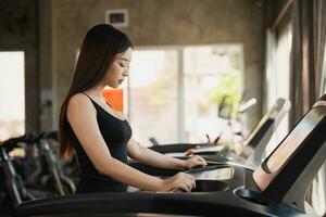 asiatique athlète sport femme coureur toucher début bouton avant faire des exercices fonctionnement sur tapis roulant dans aptitude club. cardio entraînement. en bonne santé mode de vie, femme formation dans salle de sport. sport fonctionnement concept. photo