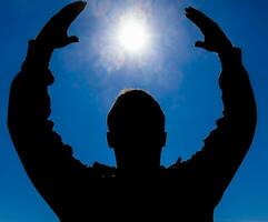 silhouette de une homme contre le Contexte de le Soleil et bleu ciel. mains sont élevé en haut à le Soleil photo