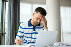 homme d'affaire Bureau travail en portant endolori tête douleur de bureau travail et séance tout journée en utilisant portable ordinateur ou carnet Souffrance mal de crâne malade ouvrier surmenage concept photo