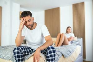 belle fille et un homme frustré assis dans son lit et ne se regardant pas. couple bouleversé s'ignorant. homme inquiet en tension au lit. jeune couple en colère après une bagarre. photo