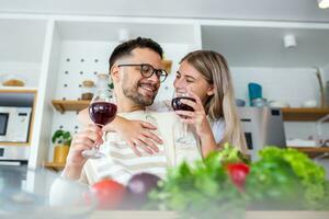 souriant Jeune couple cuisine nourriture dans le cuisine ensemble dans le cuisine, ayant une génial temps ensemble. homme et femme en riant et en buvant du vin photo