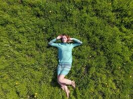 le fille mensonges dans une turquoise robe sur le pelouse. magnifique fille mensonge vers le bas de herbe photo