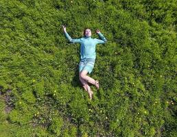 le fille mensonges dans une turquoise robe sur le pelouse. magnifique fille mensonge vers le bas de herbe photo