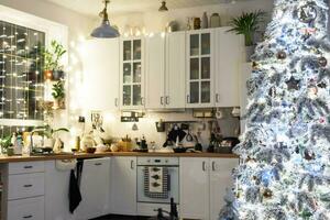 Noël décor dans blanc cuisine, de fête désordre, village intérieur avec une neigeux Noël arbre et Fée lumières. Nouveau année, Noël humeur, confortable maison. photo