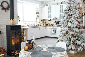 Noël décor dans blanc cuisine avec brûlant le fourneau cheminée, de fête désordre, village intérieur avec une neigeux Noël arbre. Nouveau année, Noël humeur, confortable maison. photo