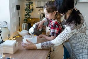 maman et fille dans la cuisine blanche pétrissent la pâte dans le bol pour le pain d'épice et les biscuits avec un mélangeur pour noël et le nouvel an. photo