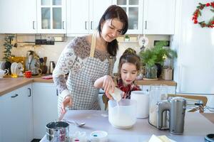 maman et fille dans le blanc cuisine sont en train de préparer biscuits, ajouter ingrédients. famille jour, préparation pour le vacances Noël, apprendre à cuisinier délicieux des pâtisseries, Couper formes en dehors de pâte avec moules photo