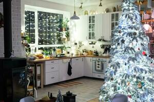 Noël décor dans blanc cuisine, de fête désordre, village intérieur avec une neigeux Noël arbre et Fée lumières. Nouveau année, Noël humeur, confortable maison. photo