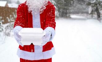 conteneurs de service de livraison de nourriture dans les mains du père noël en plein air dans la neige. promotion de la veille de noël. commande chaude prête à l'emploi, boîte en plastique jetable. restauration des vacances du nouvel an. espace de copie, maquette photo