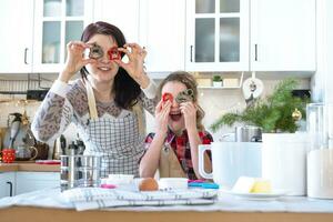 maman et fille dans le blanc cuisine sont en train de préparer biscuits pour Noël et Nouveau an. famille jour, préparation pour le vacances, apprendre à cuisinier délicieux des pâtisseries, elles ou ils tenir biscuit coupeurs comme des lunettes photo