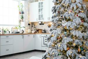 Noël décor dans blanc cuisine, de fête désordre, village intérieur avec une neigeux Noël arbre et Fée lumières. Nouveau année, Noël humeur, confortable maison. photo