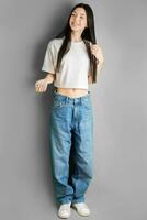 plein longueur portrait de une Jeune fille dans une blanc T-shirt et jeans. photo