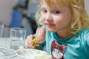 une peu fille a petit déjeuner à Accueil spaghetti avec saucisses. peu blond fille en mangeant dîner avec fourchette à table photo