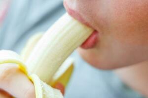 portrait de une adolescent garçon en mangeant une banane. photo de une gars bouche et lèvres avec une banane. Frais fruit. en bonne santé nourriture pour les enfants