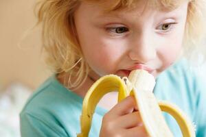 portrait de une peu fille en mangeant une banane. le concept de en bonne santé aliments. une Frais rapide casse-croûte photo
